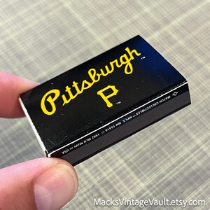May include: A black matchbox featuring the word "Pittsburgh" in yellow script and a yellow "P" logo. The matchbox is labeled "MATCH COLLECTIBLES" and "Made in USA". The Etsy shop name "MacksVintageVault.etsy.com" is visible.