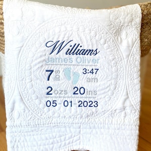 May include: White quilted baby blanket with blue embroidery. The embroidery reads "Williams James Oliver 7 lbs 2 ozs 20 ins 05-01-2023 3:47 am".