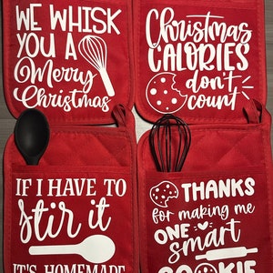 May include: Four red quilted pot holders with white text and images. The first pot holder says "We whisk you a Merry Christmas" with a whisk image. The second pot holder says "Christmas Calories don't count" with a cookie image. The third pot holder says "If I have to stir it, it's homemade" with a spoon image. The fourth pot holder says "Thanks for making me one smart cookie" with a cookie image and a rolling pin image.