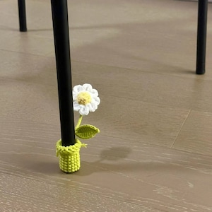Puede incluir: Un cubrepatas de silla de crochet verde con una flor de crochet blanca y hojas verdes.