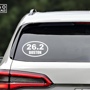 May include: White oval sticker with the text "26.2 Boston" on a silver car.