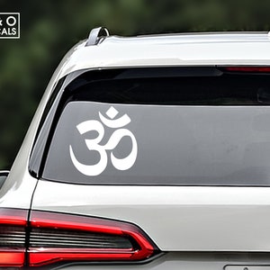 May include: White Om symbol decal on the back window of a silver car.