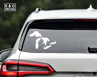 May include: White vinyl decal of the Great Lakes on the back window of a silver car. The decal is a silhouette of the five Great Lakes, with the names of each lake not included.