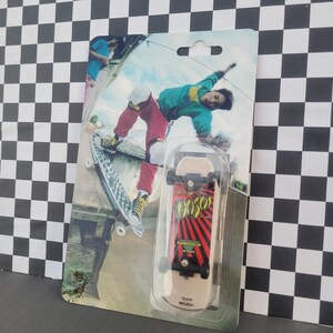 May include: A miniature skateboard toy in a clear plastic package. The skateboard has a red and black design with the word "GOOSE" in yellow. The packaging features a picture of a skateboarder performing a trick.