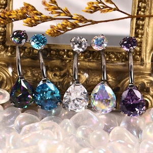 May include: Six belly button rings with different colored teardrop-shaped gemstones. The rings are made of silver and have a curved bar.