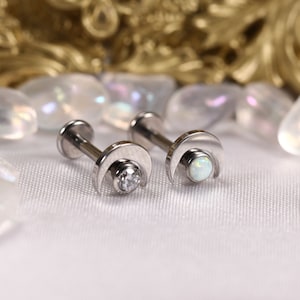 May include: Two silver crescent moon body jewelry pieces with a clear gemstone on one and a white opal on the other.