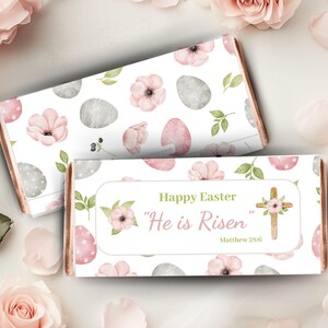 May include: White chocolate bar wrapper with a pink and gray Easter egg pattern. The wrapper has the text "Happy Easter" and "He is Risen" with a scripture reference.