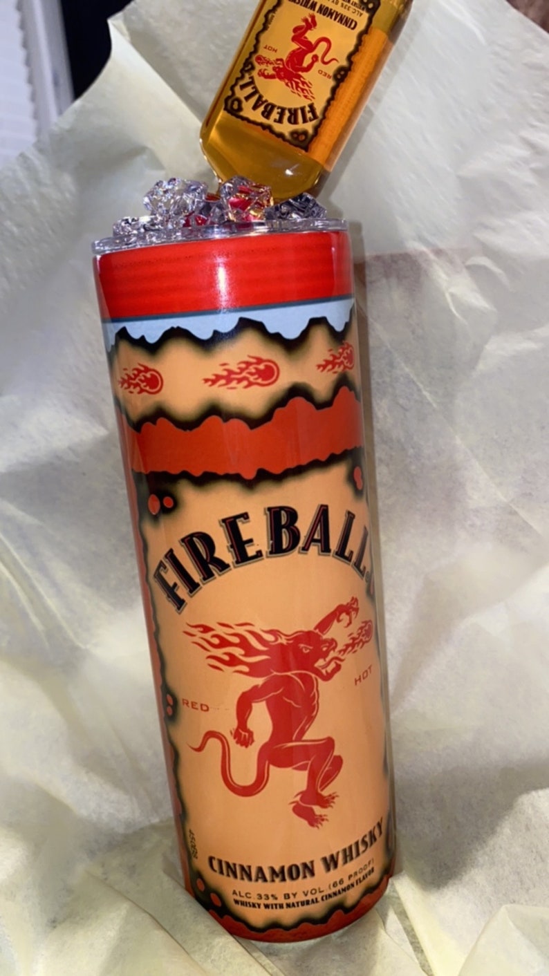 Op de afbeelding: Een aangepaste tumbler met het Fireball Cinnamon Whisky-merk. Het ontwerp bevat de merknaam, een rode duivelafbeelding en vlamaccenten. Een miniatuur Fireball-fles is boven de tumbler geplaatst.