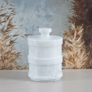 May include: White marble container with a lid. The container has two tiers and a smooth, polished finish.