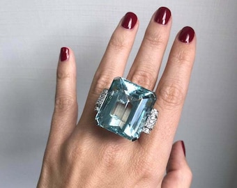 May include: A large, rectangular aquamarine gemstone ring set in platinum with smaller diamonds surrounding the main stone.