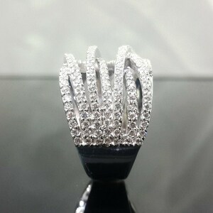 May include: A silver ring with a unique design. The ring features multiple vertical bands encrusted with small, sparkling stones. The bands are connected at the top and bottom, creating an open, cage-like structure. The base of the ring is black.