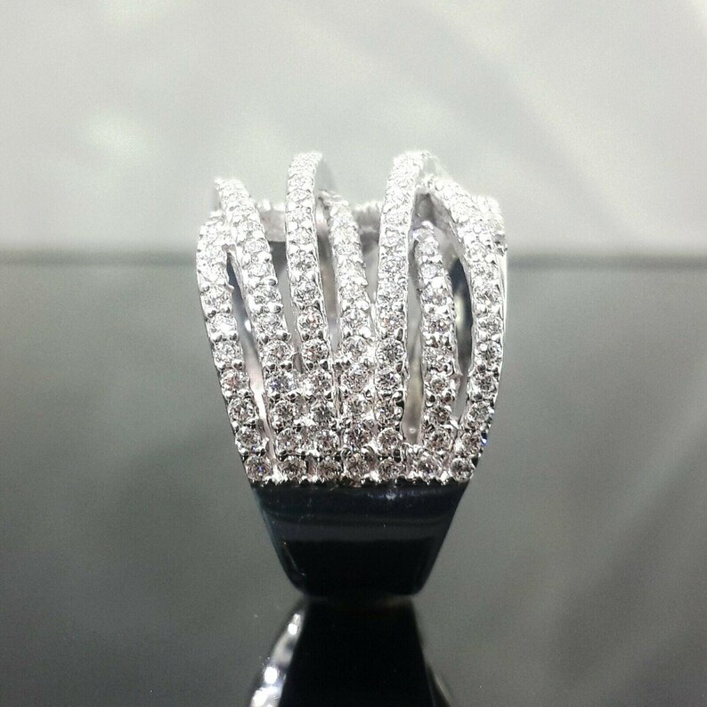 May include: A silver ring with a unique design. The ring features multiple vertical bands encrusted with small, sparkling stones. The bands are connected at the top and bottom, creating an open, cage-like structure. The base of the ring is black.