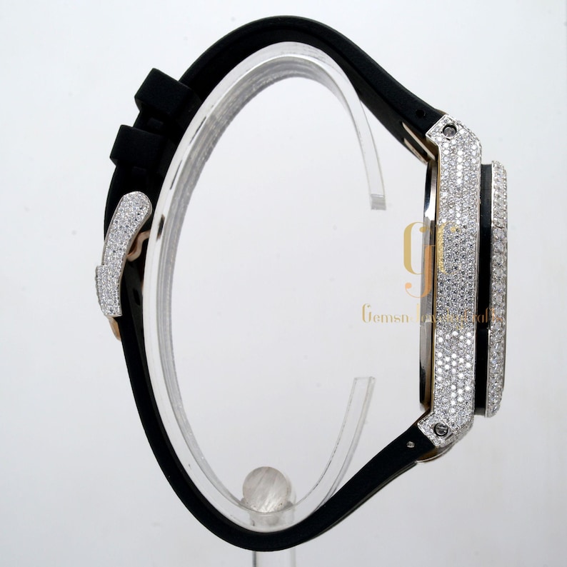 May include: A black rubber band watch with a diamond-encrusted bezel and case. The watch has a gold-tone buckle.