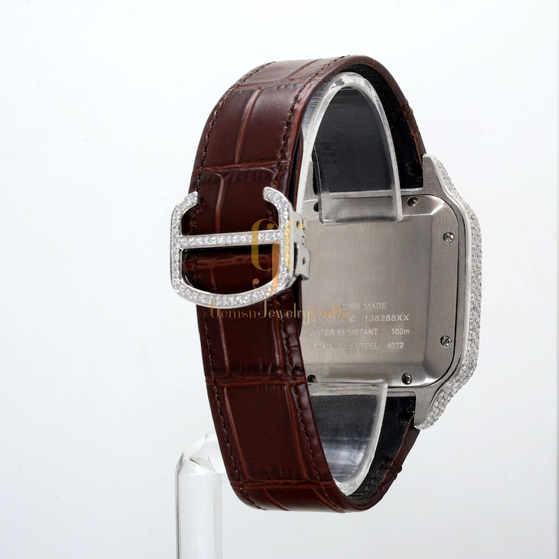 May include: A silver and diamond Cartier watch with a brown leather band. The watch face is surrounded by diamonds and the band has a diamond buckle. The watch face has the text "Swiss Made" and "Cartier" on it. The watch is water resistant to 100 meters. The watch is made of stainless steel.