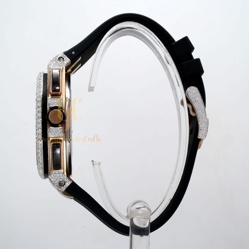 May include: A black rubber band watch with a diamond-encrusted bezel and rose gold accents. The watch has a chronograph function and a date window.