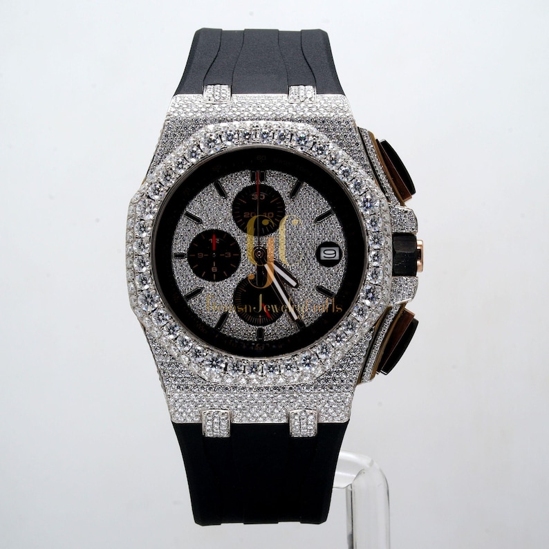 May include: A black rubber band watch with a diamond-encrusted bezel and face. The watch has a chronograph function and a date window.