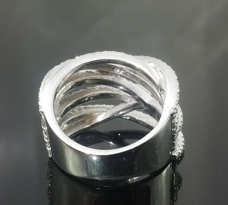 May include: A silver-colored ring with a multi-band design. The ring features multiple interwoven bands, some of which are encrusted with small, sparkling stones. The ring has a polished, reflective surface, and the design creates a layered effect.