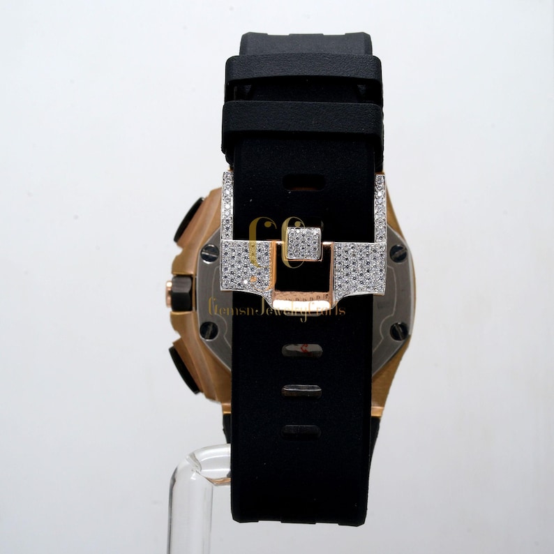 May include: A gold and black wristwatch with a diamond-encrusted clasp. The watch has a black rubber strap and a round face.