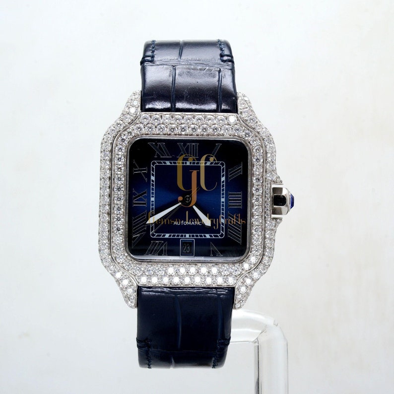 May include: A diamond-encrusted wristwatch with a blue face and Roman numeral hour markers. The watch has a black leather band and a sapphire crystal.