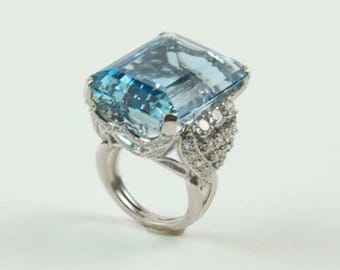 May include: A large, rectangular aquamarine gemstone ring. The light blue gemstone is set in a silver band with smaller accent diamonds. The ring has an ornate, detailed design.
