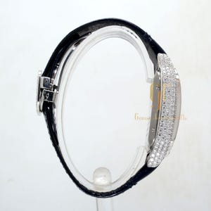 May include: A silver watch with a black leather band. The watch face is covered in diamonds.