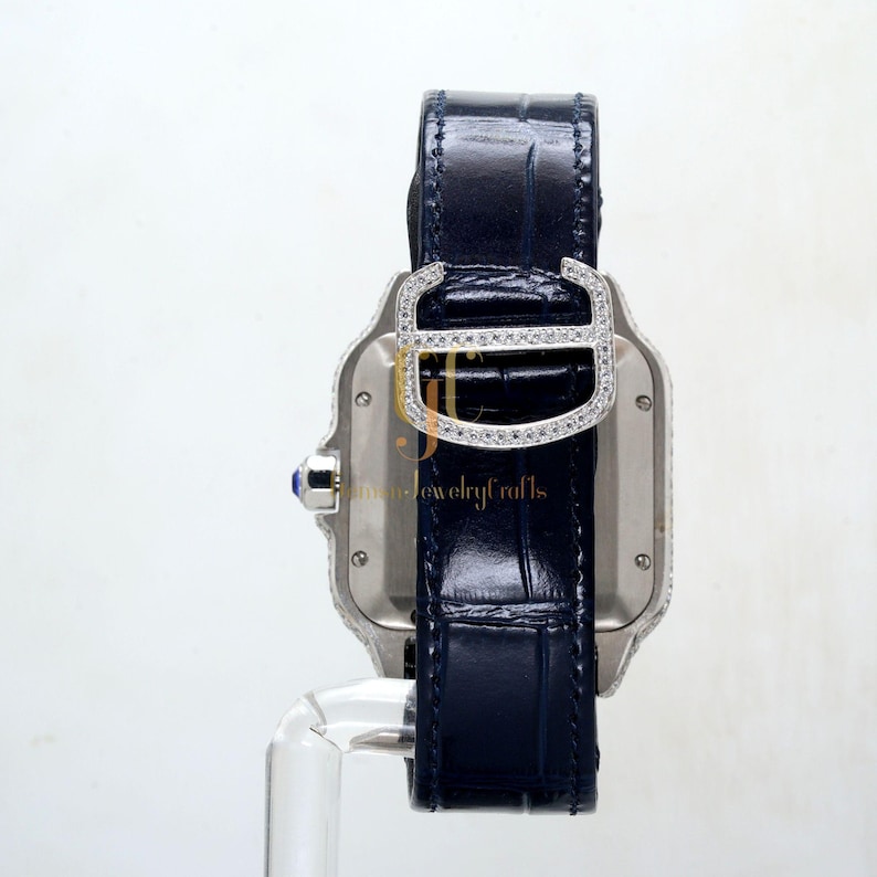 May include: A silver watch with a diamond-encrusted bezel and a blue leather strap. The watch has a square face and a rectangular case.