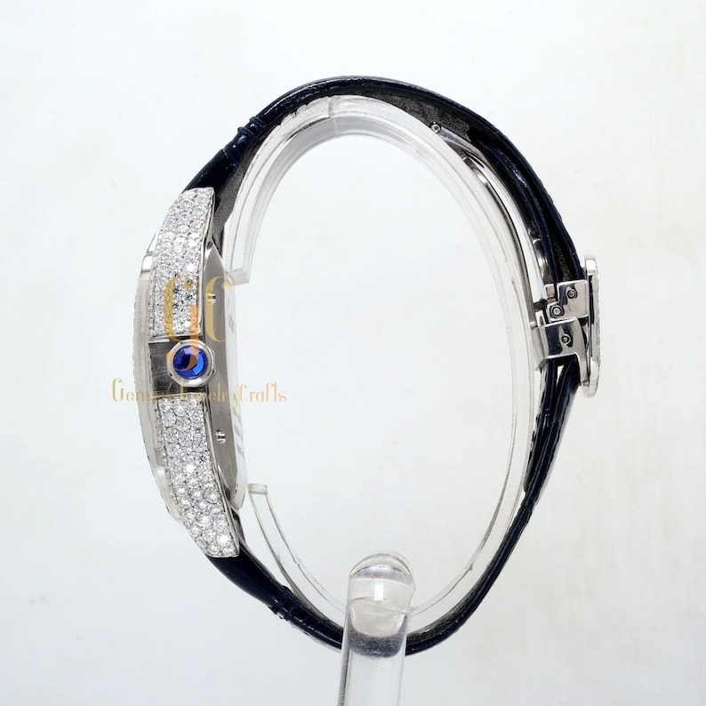 May include: A silver wristwatch with a black leather band and a diamond-encrusted bezel. The watch face has a blue sapphire cabochon at the 12 o'clock position.
