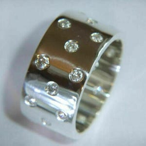May include: A wide, polished silver ring with multiple round, clear gemstones set into the band. The gemstones are evenly spaced around the ring, creating a sparkling effect. The ring is a statement piece of jewelry.