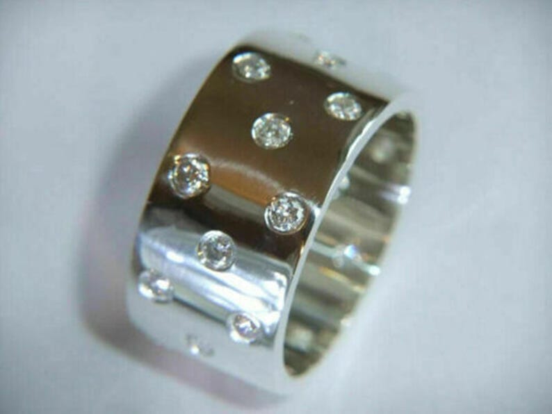 May include: A wide, polished silver ring with multiple round, clear gemstones set into the band. The gemstones are evenly spaced around the ring, creating a sparkling effect. The ring is a statement piece of jewelry.