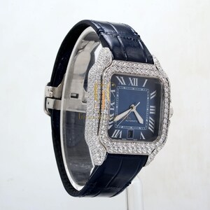 May include: A silver watch with a blue face and diamond accents. The watch has a black leather band and a square face. The face of the watch has Roman numeral hour markers and the word "Automatic" printed on it.