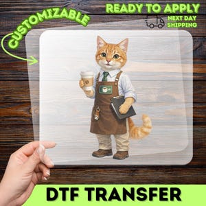 May include: A DTF transfer sheet featuring an orange tabby cat dressed as a barista, wearing a light blue shirt, green tie, and brown apron. The cat holds a coffee cup and a black clipboard. The design includes a small coffee cup icon on the apron.