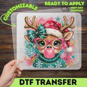 May include: A clear DTF transfer sheet featuring a reindeer illustration wearing a red Santa hat, a teal sweater with white snowflakes, a teal bow, and pink glasses while blowing a pink bubble gum bubble, surrounded by colorful festive splatters.