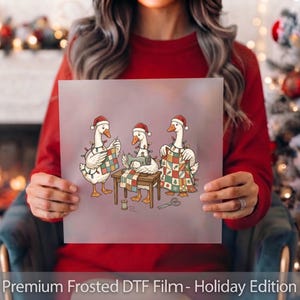 May include: A frosted film sheet featuring a graphic illustration of three white geese wearing red Santa hats and wrapped in colorful Christmas lights. The geese are sewing a patchwork quilt with a sewing machine on a wooden table.