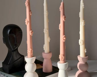 May include: Four candles with floral designs, two are pink and two are white. The candles are in white and pink candle holders. The candles are on a magazine with the word "Kinfolk" printed on the cover.