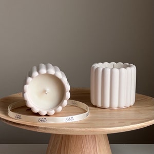 May include: Two white ceramic candles with a ribbed design. The candles are on a wooden pedestal with a white ribbon that says "Etelle" on it.