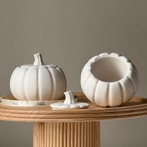 Puede incluir: Contenedores blancos de cerámica con forma de calabaza con tapas, uno abierto, sobre una bandeja de madera. Los contenedores tienen lados acanalados y un asa en forma de tallo. Una cinta con la palabra "Estelle" está en la bandeja.