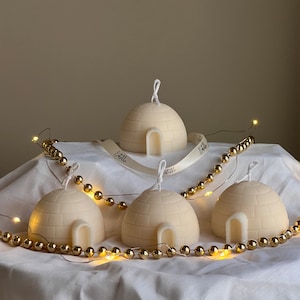 Puede incluir: Cuatro velas blancas en forma de iglú con una superficie texturizada. Las velas están dispuestas sobre una superficie blanca con cuentas doradas y una cinta blanca con el texto "Etoile" en ella.