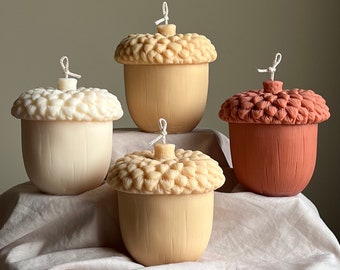 May include: Four acorn-shaped candles in different colors. The candles are made of wax and have a textured surface. The candles are arranged in a row on a white surface.