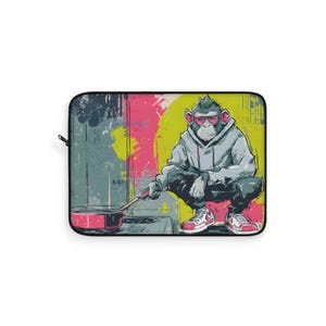 May include: Laptop sleeve featuring a colorful illustration of a monkey wearing a hoodie and sneakers, cooking with a pan. The background has a graffiti-style design with pink, yellow, and blue paint splatters.