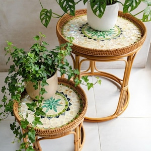 May include: Two round side tables constructed from light brown woven rattan with circular tops featuring inlaid mosaic tiles in shades of cream, white, and green. Each table has a sturdy frame with curved legs and a circular base support.