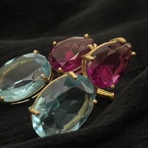 Peut inclure: Une paire de boucles d'oreilles avec des pierres ovales bleu clair facettées et une paire de boucles d'oreilles avec des pierres rose foncé en forme de poire facettées, montées sur des griffes en métal doré. Les bijoux sont disposés ensemble.