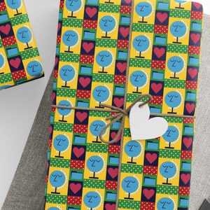 Puede incluir: Varios regalos envueltos con papel estampado colorido. El diseño presenta caras azules, corazones rojos y lunares verdes sobre un fondo amarillo. Cada regalo está atado con hilo y una etiqueta blanca.