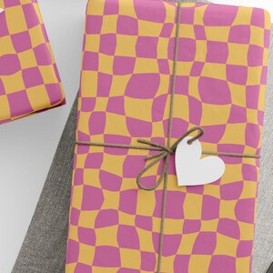 May include: Gift-wrapped presents with a wavy, checkerboard pattern in pink and yellow. Each package is tied with twine and a white paper tag in the shape of a star or heart. A spool of white thread is in the lower left corner.