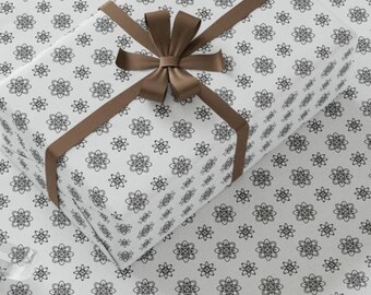 May include: A white gift box wrapped in white paper with a black repeating pattern of stylised flowers. The box is tied with a brown ribbon and bow.