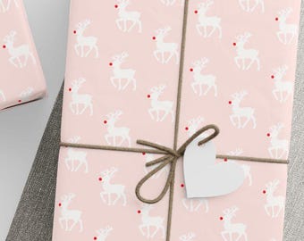 Peut inclure: Plusieurs cadeaux emballés avec du papier rose à motifs de rennes blancs et de nez rouges. Les cadeaux sont attachés avec de la ficelle marron et ornés d'étiquettes blanches en forme d'étoile et de cœur. Une pelote de ficelle et des ciseaux sont également visibles.