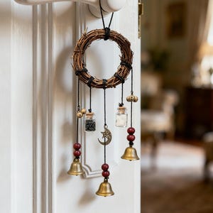 May include: A circular wreath crafted from woven twigs, featuring hanging charms such as small glass bottles, brass bells, and a crescent moon pendant. The wreath is suspended from a white door handle.