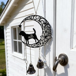 Könnte beinhalten: Schwarzer Metall-Windspiel mit einer Hundesilhouette auf einem Mond mit floralen Details. Es hat drei Bronzeglocken und einen Kristallanhänger. Der Hund hat das Wort "Bud" auf seiner Seite. Das Windspiel hängt an einer Kette.