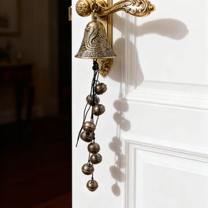 May include: Ornate brass door hardware with a bell and hanging spheres. The door handle and plate have detailed scrollwork. A bell with an engraved design hangs from a chain, with multiple small spheres suspended below.