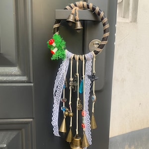 Puede incluir: Un atrapasueños blanco y marrón con una variedad de encantos, incluyendo campanas, cuentas y un cristal azul. El atrapasueños está colgado de una puerta.