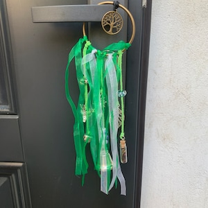 May include: A green and white dream catcher with a small glass bottle charm hanging from it. The dream catcher is attached to a door with a metal ring. The dream catcher has a small tree design in the centre.